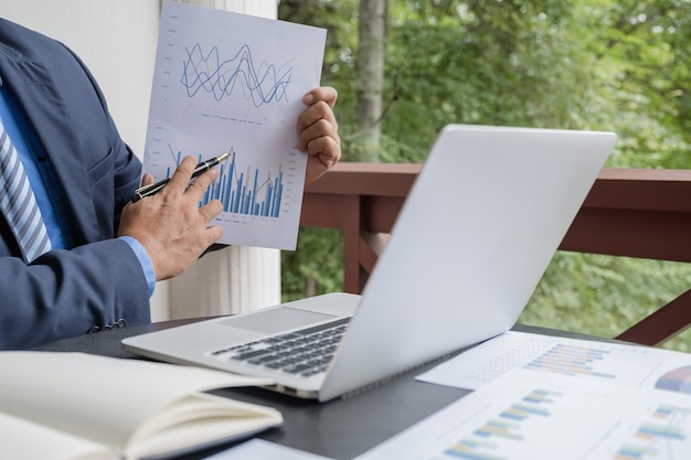 Businessman holding pen analysis graph with laptop at home office for setting business goals