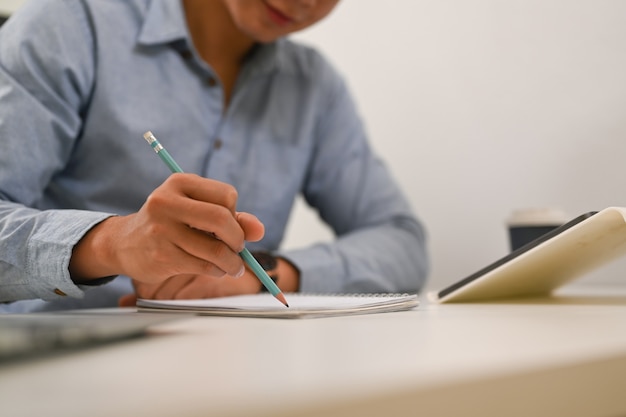 businessman holding pencil writing on note book at office desk.