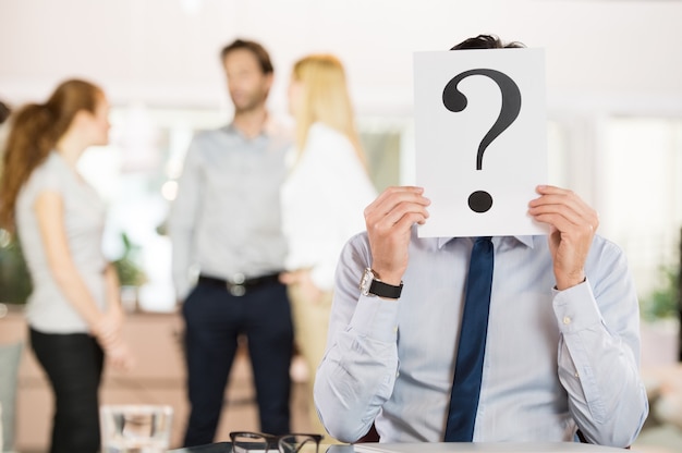 Photo businessman holding a question mark sign in front of his face.