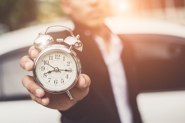 Businessman holding the retro clock in front of the white car