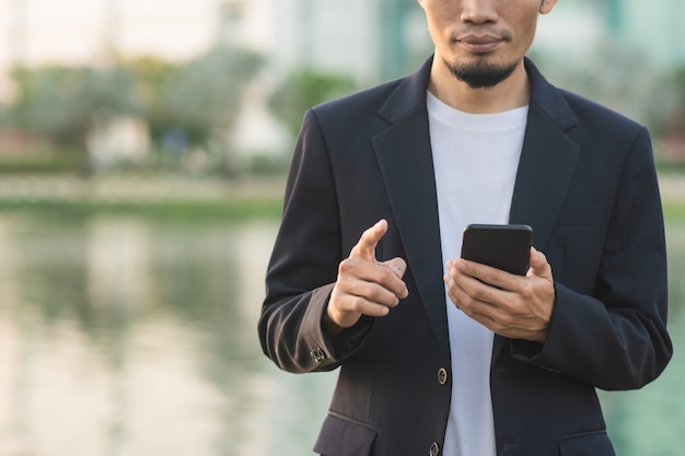 Uomo d'affari che tiene smartphone parco cittadino all'aperto urbano