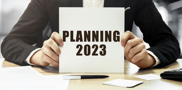 オフィスの背景にテキスト「計画 2023 年」が記載された白いカードを保持している実業家