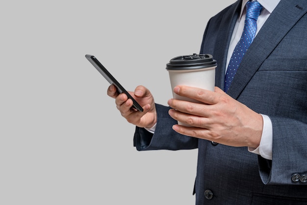 A businessman holding a white paper cup and a smartphone. With copy space.