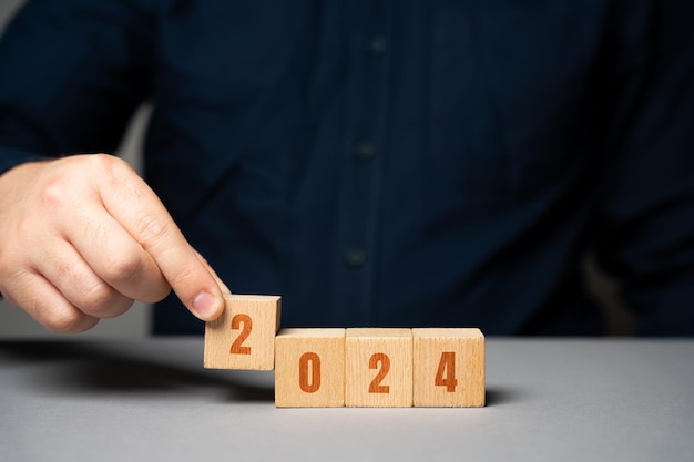 Businessman holding wooden blocks 2024 Business plan and strategy concept Planning Targets