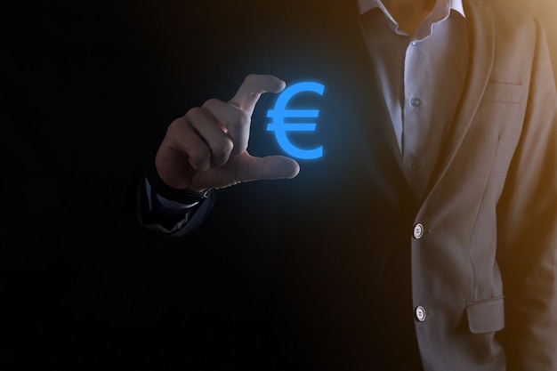 Бизнесмен держит значки монет евро или евро на темном фоне тона