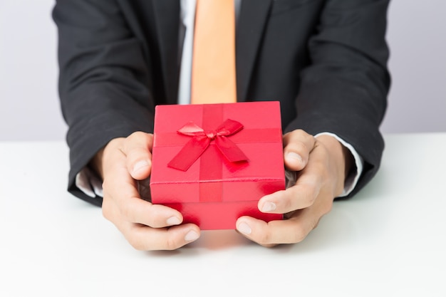 Businessman holds out the gift red box, isolated background