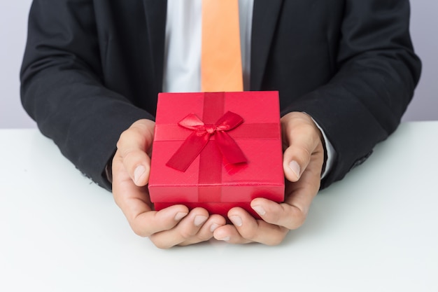 Бизнесмен протягивает подарок красной коробке, изолированный фон