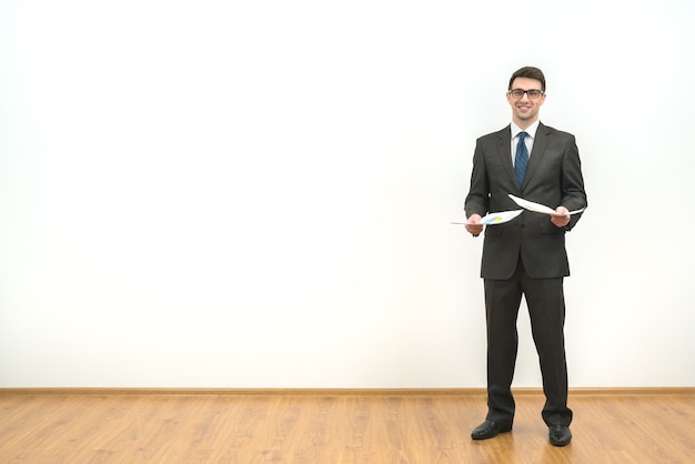 The businessman holds papers on the white wall background