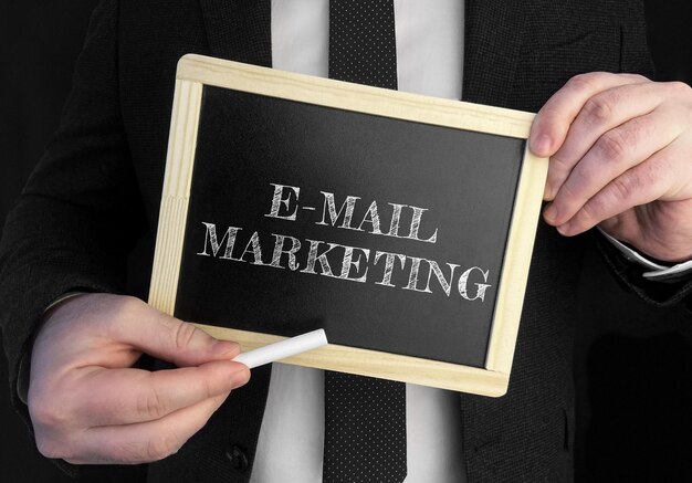 A businessman holds up a chalkboard with text Email marketing