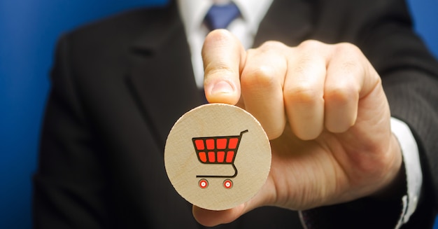 Businessman holds a wooden block with the image of a supermarket cart - shopping trolley.