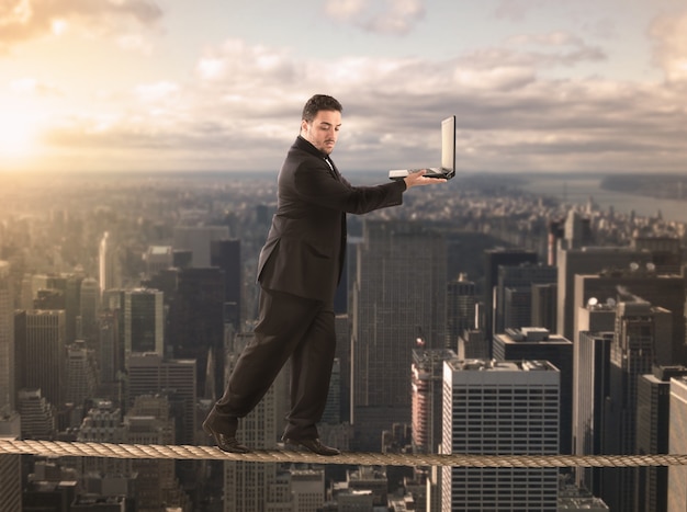 Businessman is balancing on a rope and holds a laptop