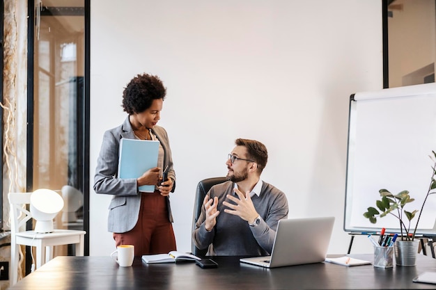 A businessman is having discussion with multicultural associate while sitting in office at firm