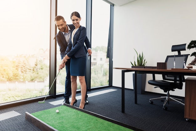 Businessman is teaching his secretary to play mini golf.