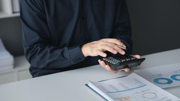 A businessman is using a calculator to calculate financial numbers he is sitting in his private office the businessman examines the financial data from the corporate finance chart