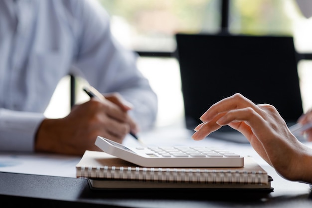 A businessman is using a white calculator to calculate financial numbers he is sitting in his private office the businessman examines the financial data from the corporate finance chart