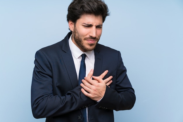 Businessman over isolated blue wall having a pain in the heart
