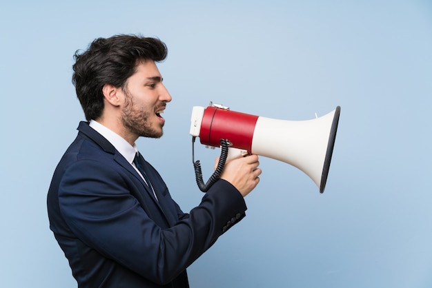 businessman over isolated blue wall shouting through a megaphone