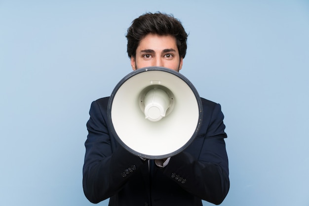 Businessman over isolated blue wall shouting through a megaphone
