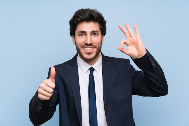 Businessman over isolated blue wall showing ok sign and thumb up gesture