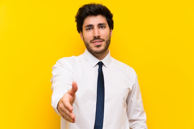 Businessman on isolated yellow background handshaking after good deal