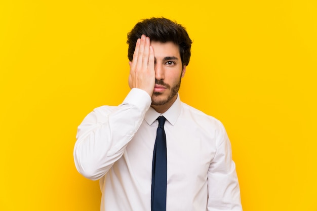 Businessman on isolated yellow covering a eye by hand