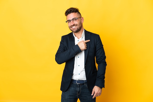 Businessman over isolated yellow wall pointing to the side to present a product