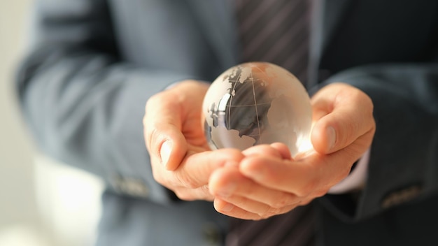 Businessman in jacket holding glass ball with world map closeup