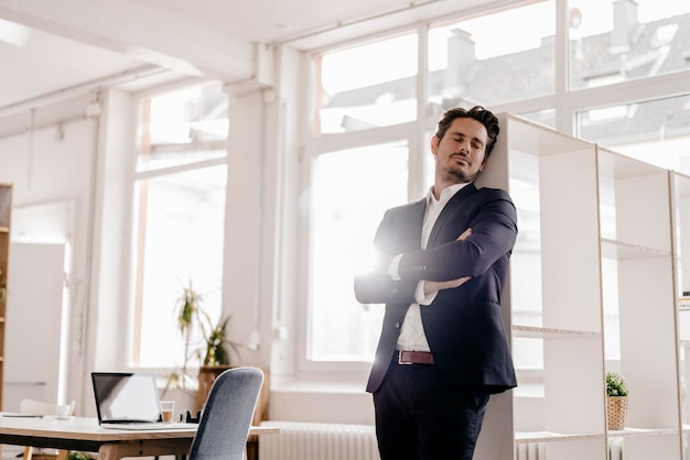 Businessman leaning against shelf in office