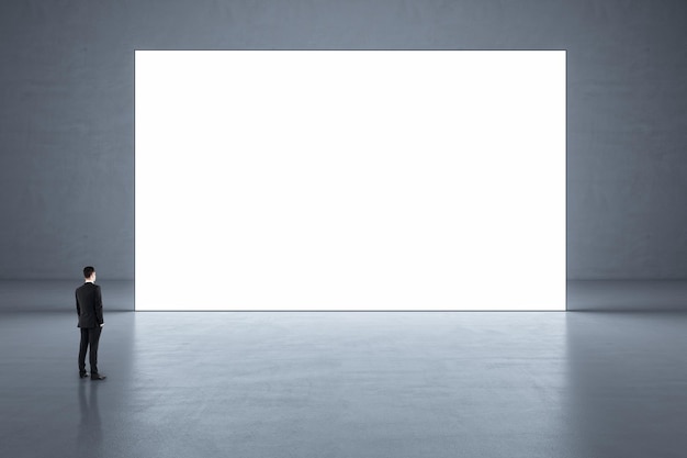 사진 광택 콘크리트 바닥이 있는 추상 빈 갤러리 홀에서 큰 흰색 빈 포스터를 보고 있는 사업가