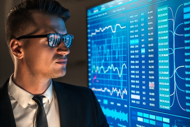 The businessman looking on the blue screen in the dark office