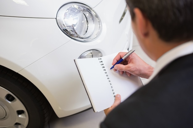 Businessman looking at car while writing on clipboard