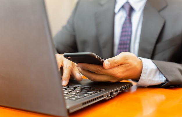 Businessman looking at cell phone and work on laptop.