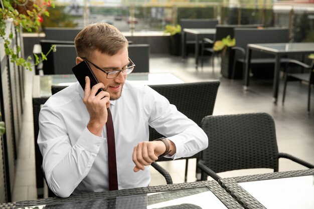 Businessman looking at his watch while talking by phone in cafe