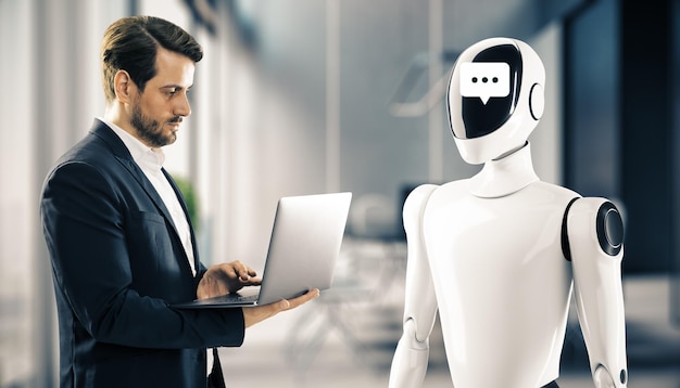 オフィス環境でチャットシンボルを顔にしたヒューマノイドロボットの前に立ってラップトップを見ているビジネスマン