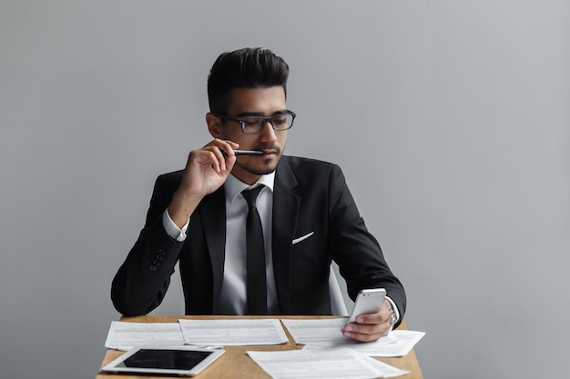 Businessman looking at mobile phone with a pen in his mouth