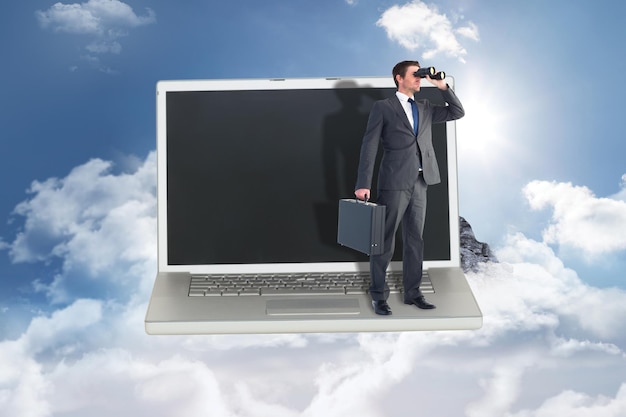 Бизнесмен смотрит в бинокль на горную вершину сквозь облака