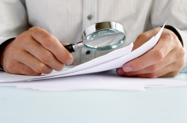 Businessman looking through a magnifying glass to documents