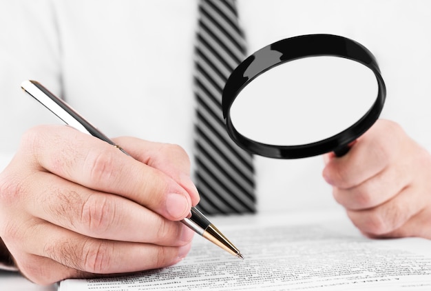 Businessman looking through a magnifying glass to documents