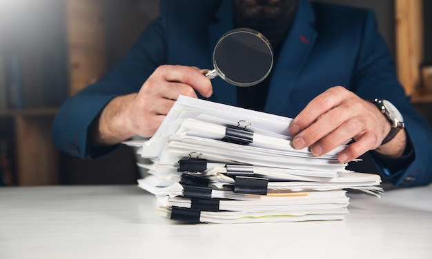 Businessman looking through a magnifying glass to documentsxDxA