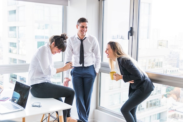 Uomo d'affari che esamina la donna di affari due che ride nell'ufficio