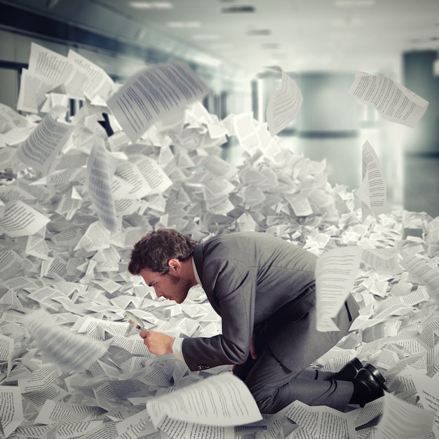 Businessman looking with magnifying glass in the middle of a flood of sheets