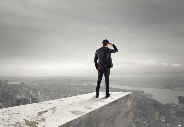 Businessman looks at the city from the roof above the city