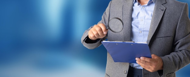 Businessman looks at papers with a magnifying glass