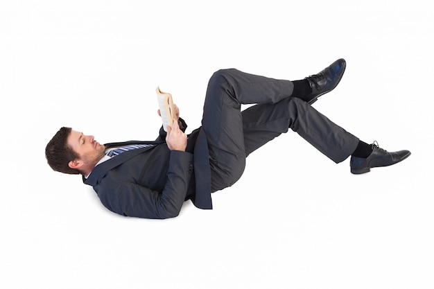 Businessman lying on the floor reading a book