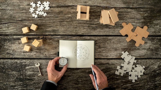 Businessman making plan and business strategy decisions as he sketches a compass he is holding into his notebook.