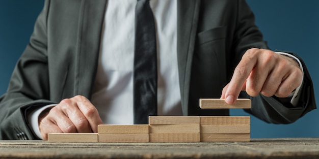 Businessman making a stairway like structure of wooden pegs in a conceptual image of business progress and promotion.