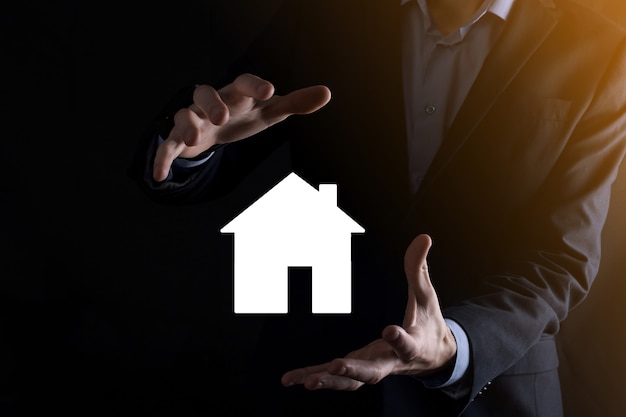 Businessman male hand holding house icon on blue wall. Property insurance and security concept.Real estate concept.Banner with copy space.