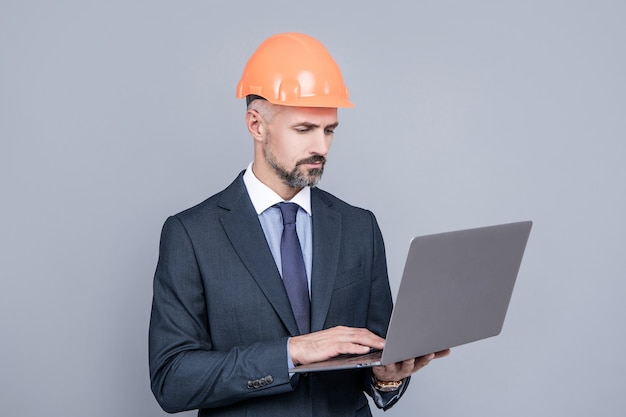 Uomo d'affari nella costruzione del casco utilizzando il computer, conferenza online di sicurezza.