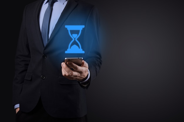 Businessman man holds in hand hourglasses icon. Time expires. A reminder to action.