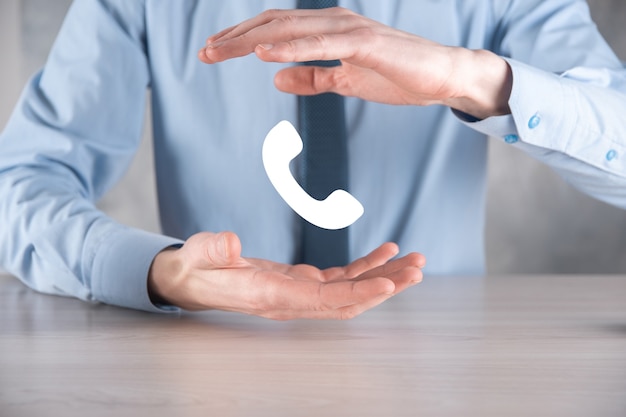 Businessman man in a shirt with a tie on gray wall hold phone icon.Call Now Business Communication Support Center Customer Service Technology Concept.